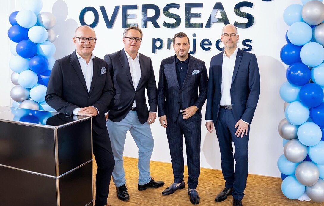 (Von links:) Hans-Bernd Effing (Geschäftsführer der Overseas Projects), Dominik Lucius (CFO der FMS), Navid Thielemann (CEO der ThielemannGroup) und Heiko Voigt (CEO der FMS) vor einer Stellwand mit dem Overseas Projects-Schriftzug und vor zwei mit Luftballons geschmückten Säulen