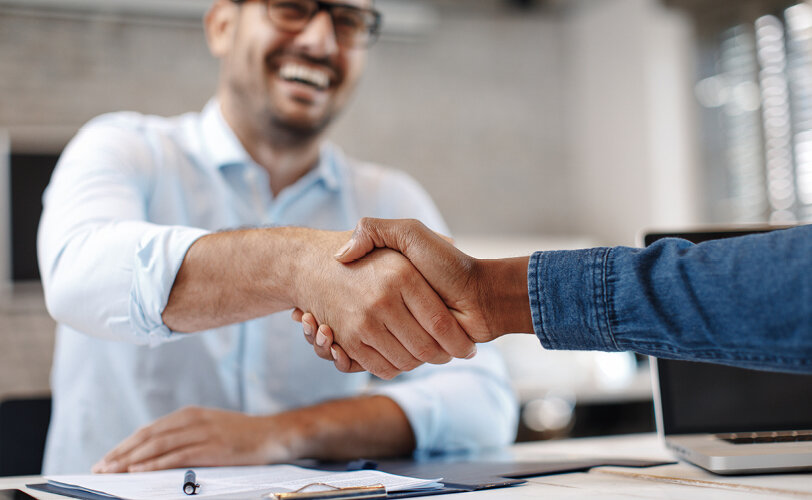 Foto: Mann im Businessoutfit schüttelt jemandem die Hand und lächelt