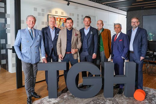 Gruppenfoto des fünfköpfigen Beirats und des Management-Teams der ThielemanGroup mit den hüfthohen Buchstaben TGH davor