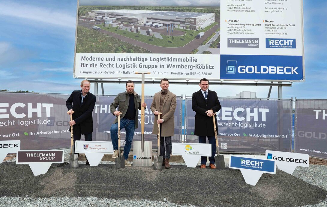 Vier Männer vor dem Bauschild mit einem Spaten